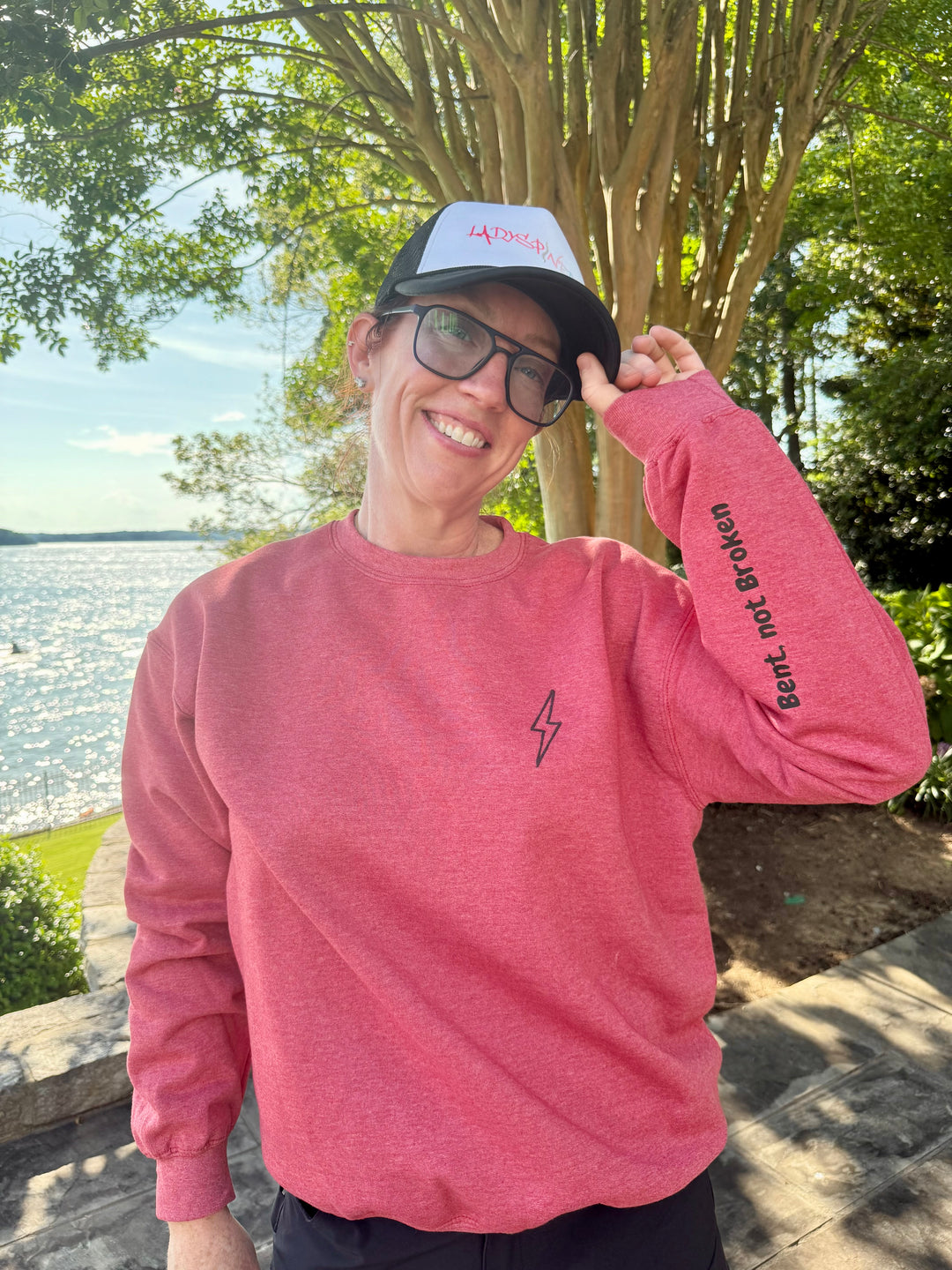 A smiling Dr. Betsy Grunch wearing her red Bent Not Broken Scoliosis Crewneck Sweatshirt and a Ladyspinedoc trucker hat.