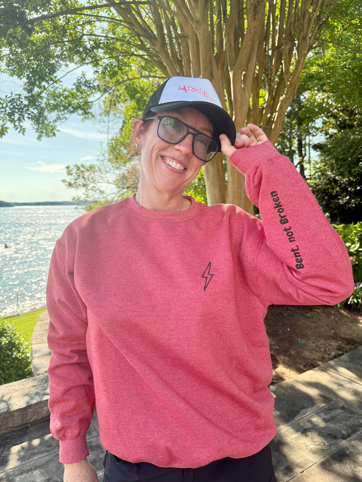 A smiling Dr. Betsy Grunch wearing her red Bent Not Broken Scoliosis Crewneck Sweatshirt and a Ladyspinedoc trucker hat.