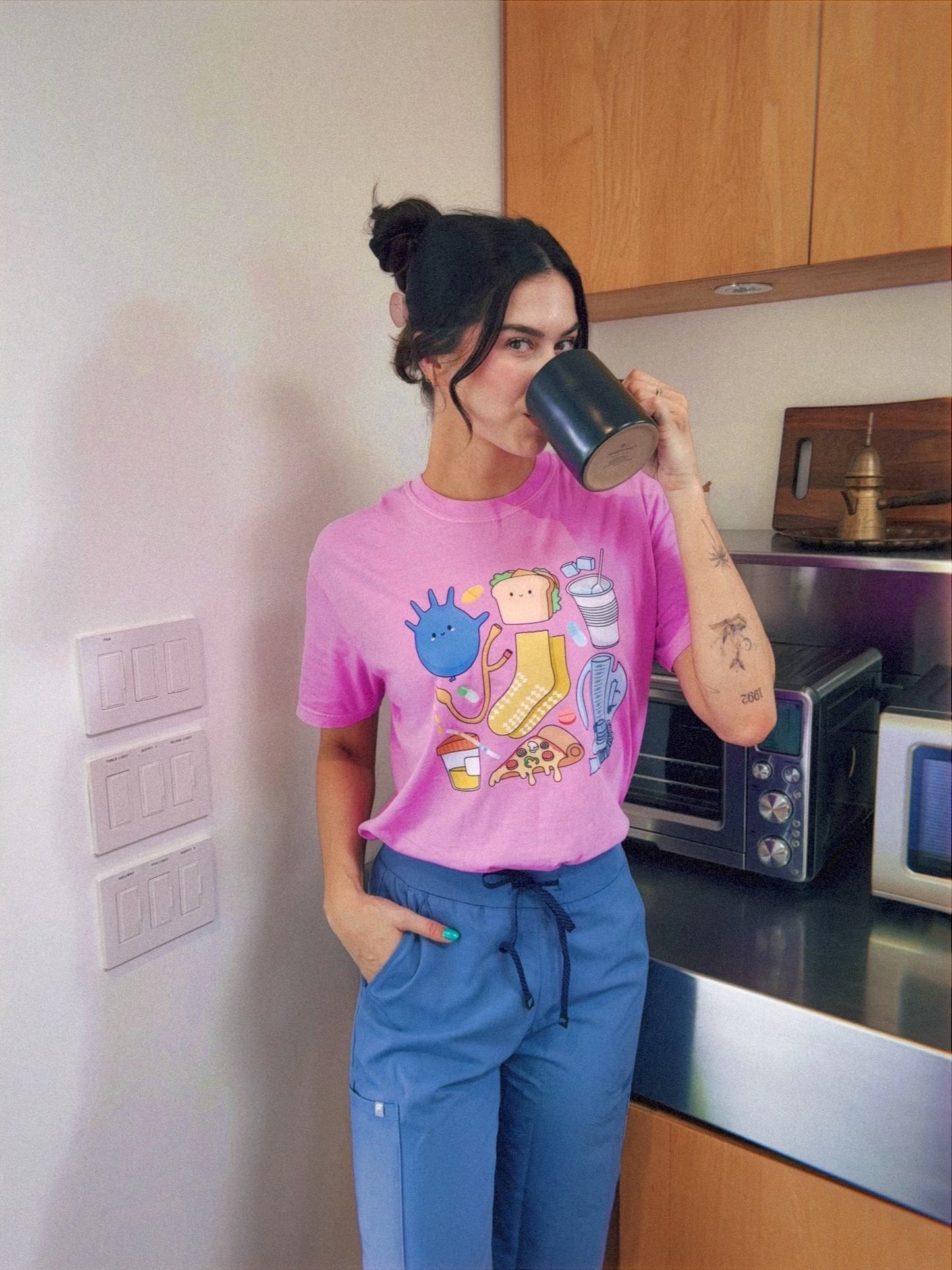Scrubhacks drinking out of a mug and wearing her purple Nurse tee shirt designed by Her Crescent & Co