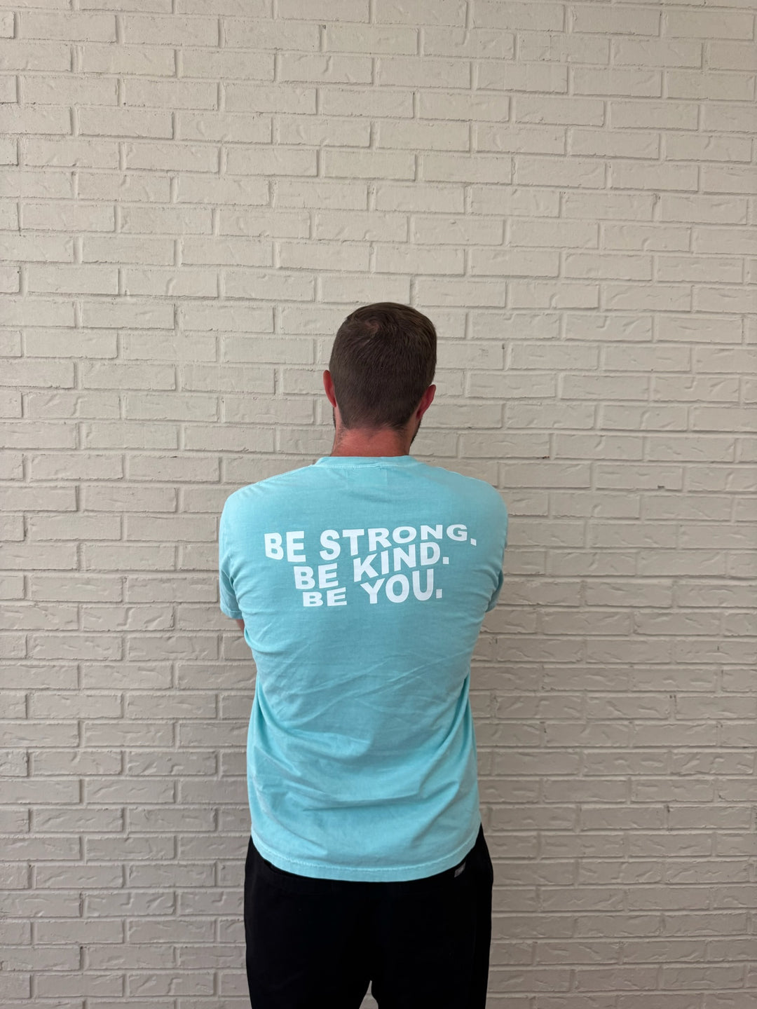 Back of male model wearing the BE YOU Tee Shirt, showing the BE STRONG. BE KIND. BE YOU. motto on the back.