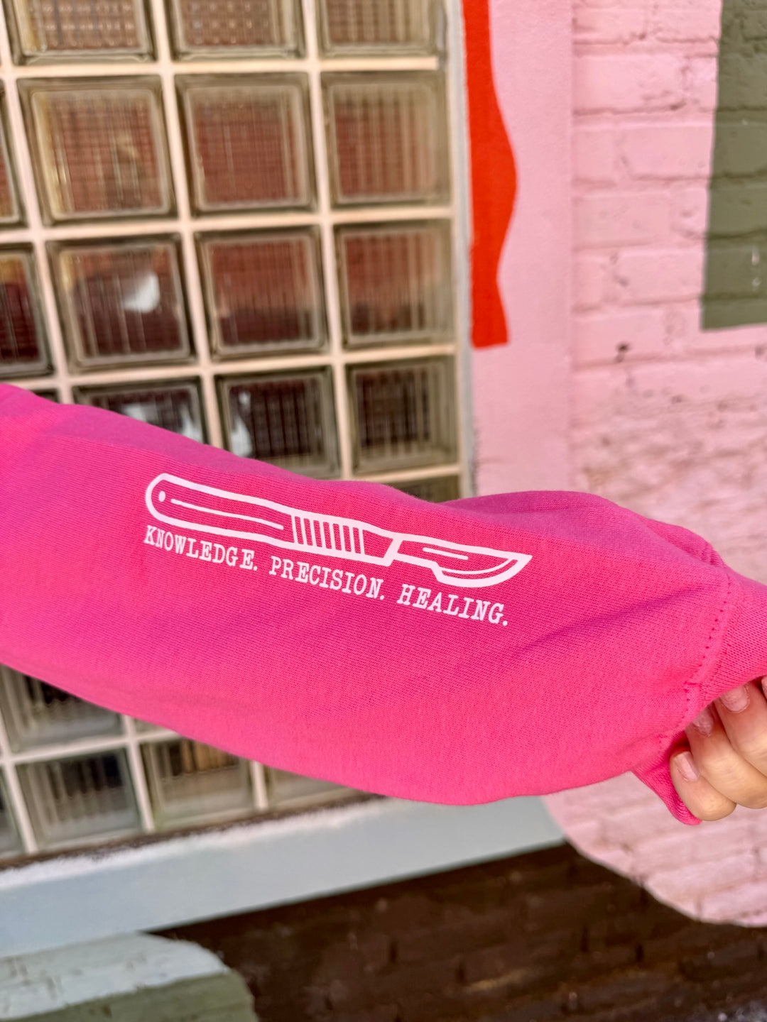 Pink sleeve with a white scalpel graphic  anchored by the text KNOWLEDGE. PRECISION. HEALING.