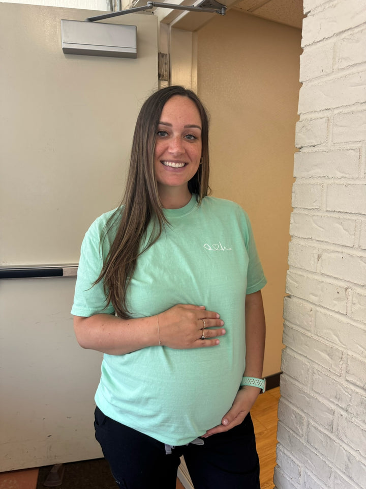 Pregnant woman wearing the Ladyspinedoc x Dr. Beachgem Heart of Medicine Tee Shirt in Island Reef Green Short Sleeve with Dr. Beachgem's Signature Logo