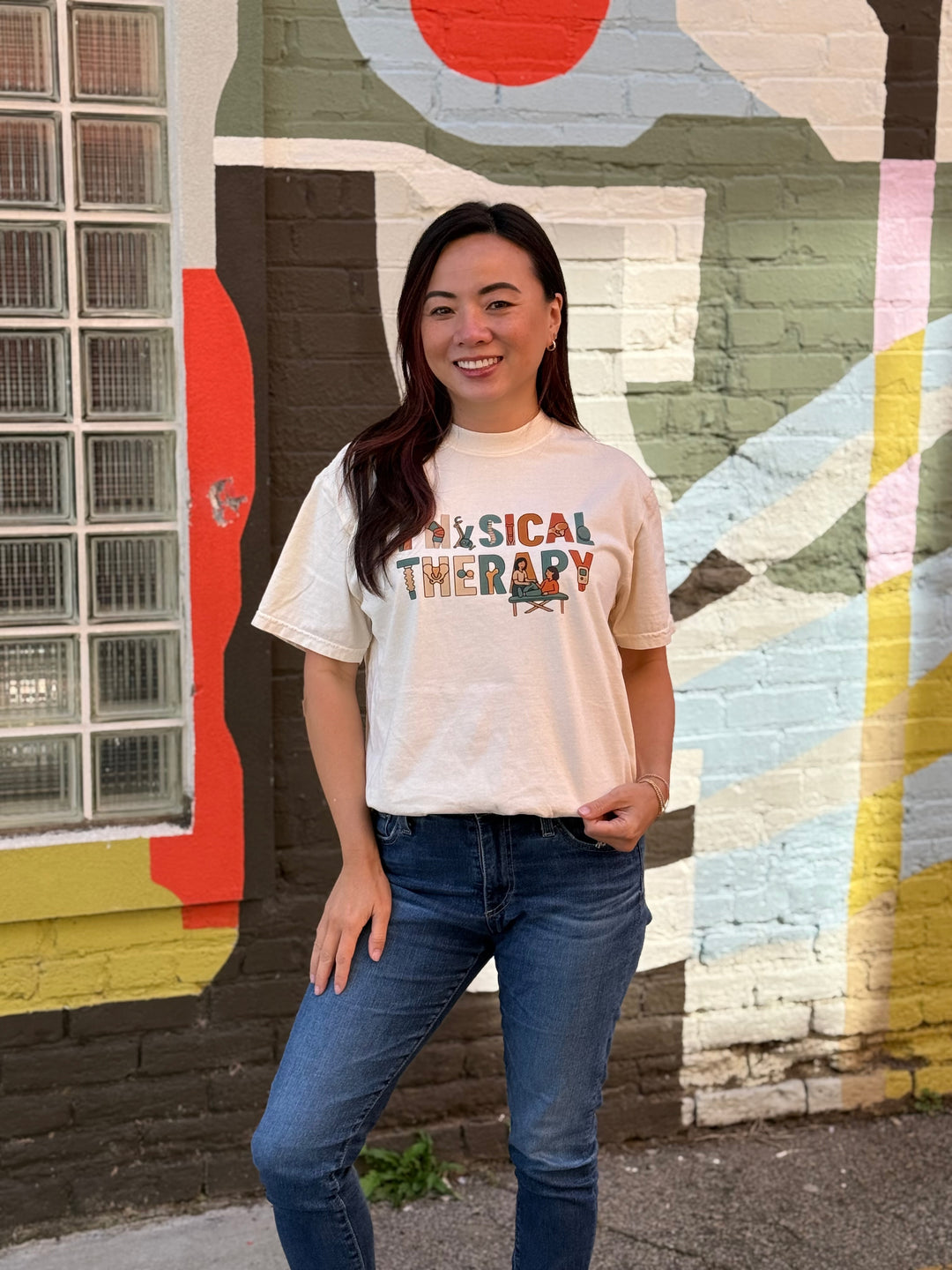 Woman wearing a 'Physical Therapy' t-shirt in front of a colorful mural.