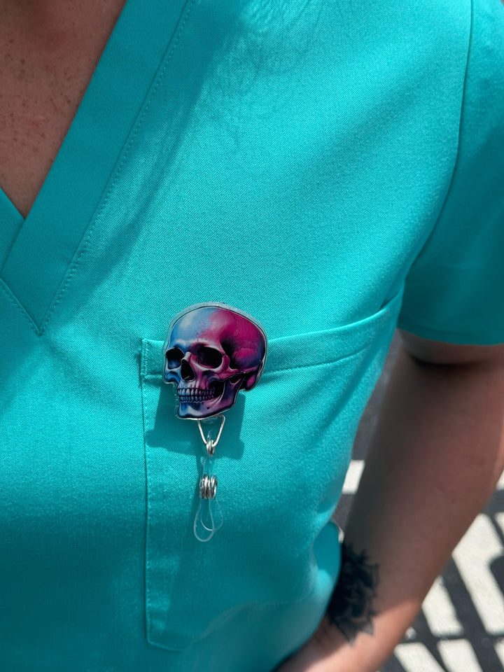 Close up view of Super Skull Badge Reel - Retractable with Alligator Clip and Colorful Skull Design clipped on front pocket of aqua scrub shirt