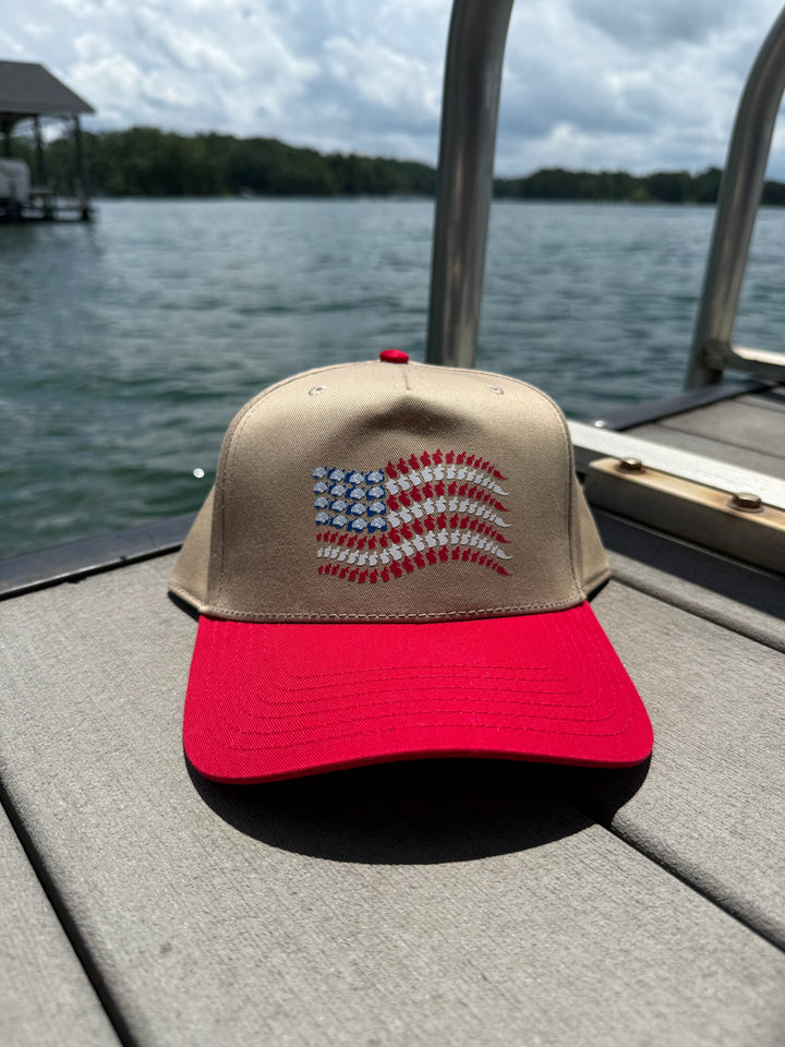 Stars, Stripes & Synapses tan and red ball cap with brain and spine American flag design sitting on a dock by the water.