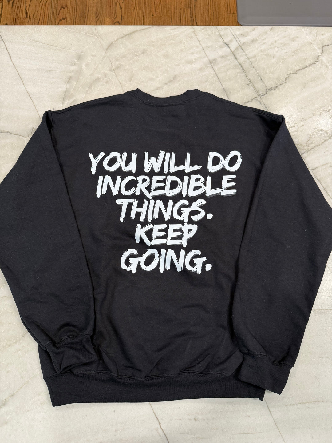 Back flat lay of the black Incredible Youth Crewneck Sweatshirt with bold white brushstroke message: "YOU WILL DO INCREDIBLE THINGS. KEEP GOING."