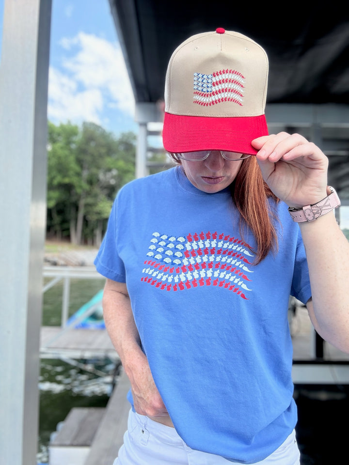 Ladyspinedoc tipping the brim of the tan and red ball cap with brain and spine flag, wearing the matching Stars, Stripes & Synapses tee.