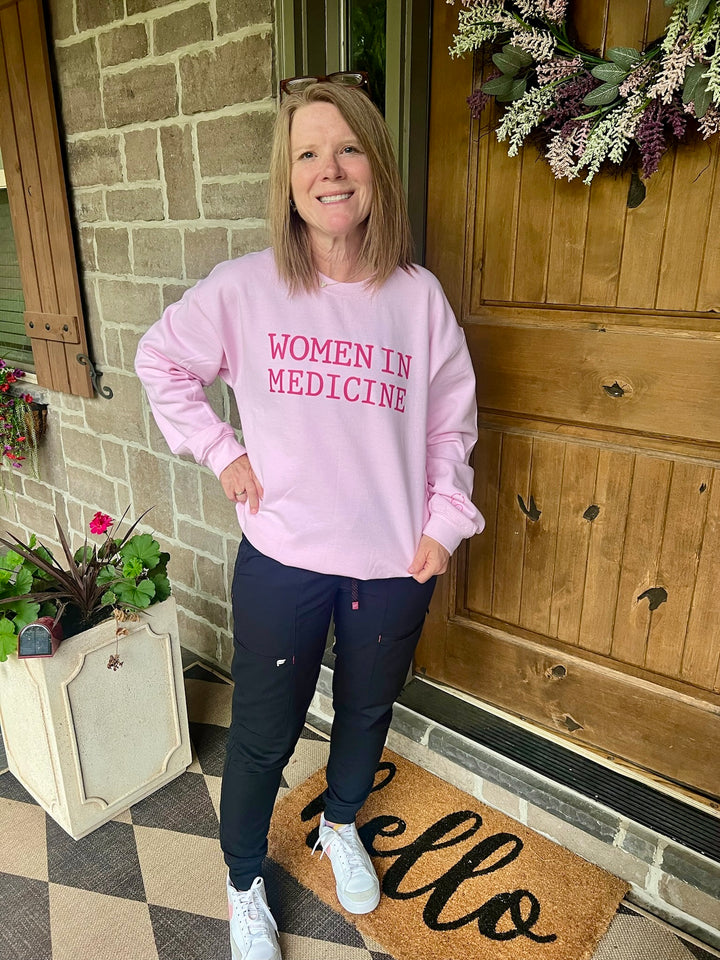 Woman wearing light pink “WOMEN IN MEDICINE” sweatshirt