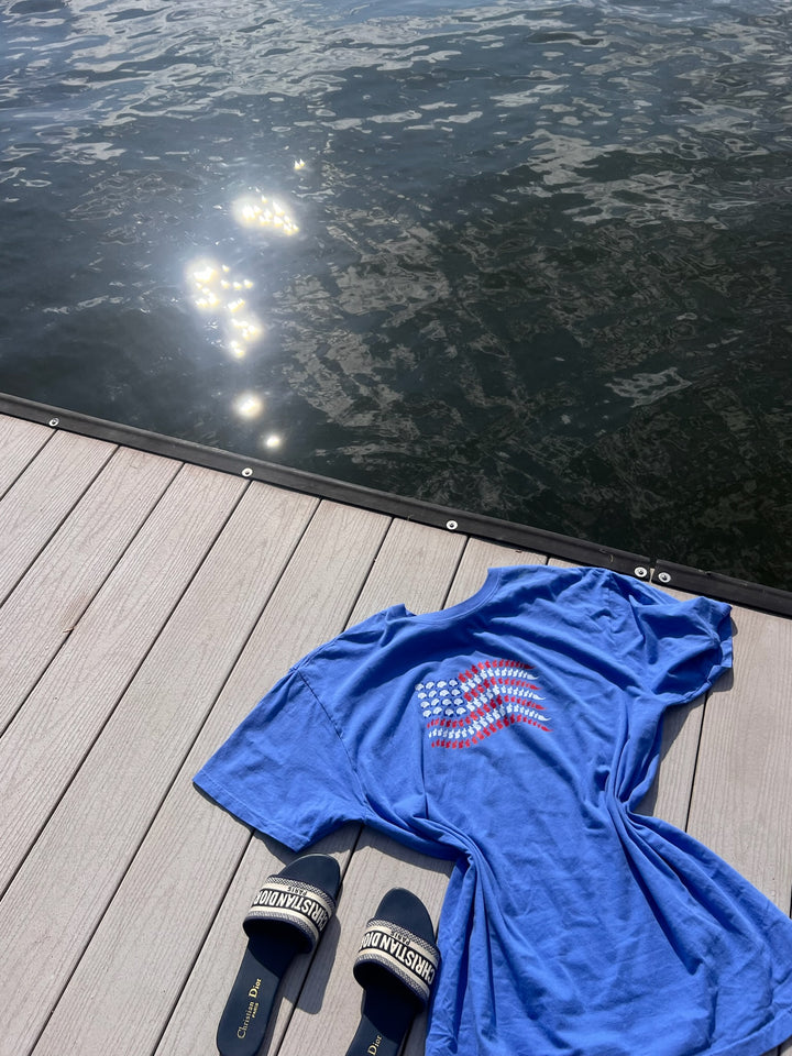 The Ladyspinedoc Stars, Stripes & Synapses tee featuring brains and spines as a patriotic flag, laying on a dock by the lake.