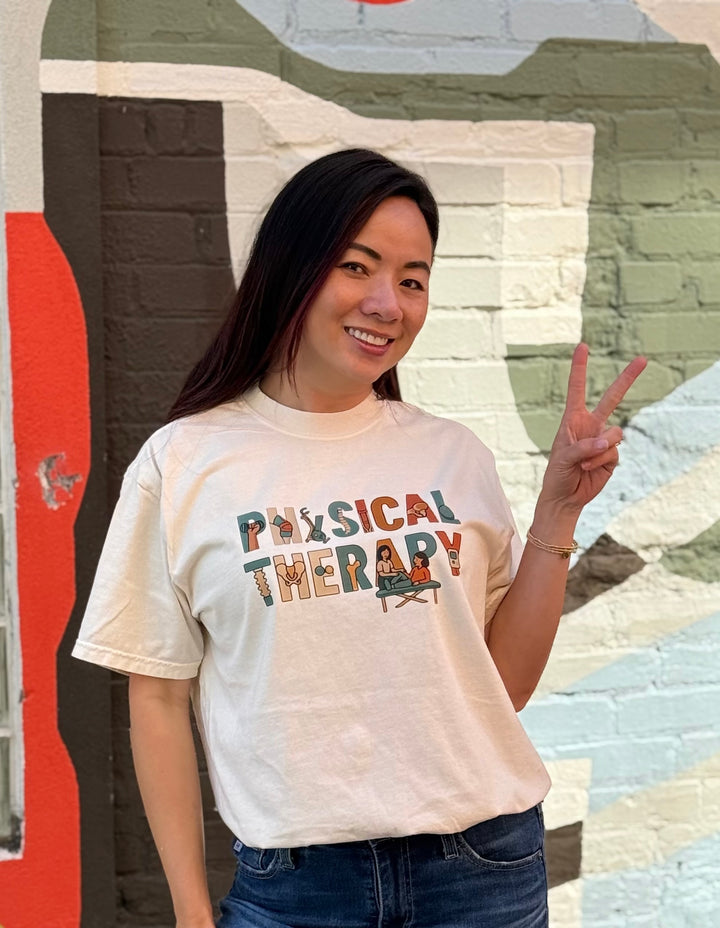Woman wearing an ivory-colored 'Physical Therapy' t-shirt in front of a colorful mural.