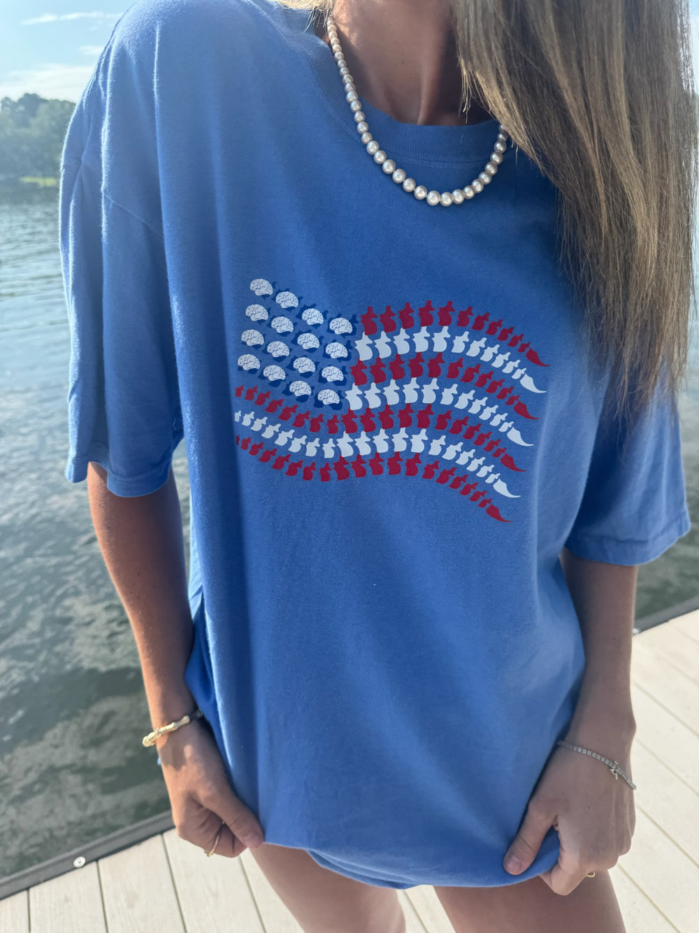 Model wearing blue Stars, Stripes & Synapses tee featuring brains and spines as a patriotic flag, by the lake.