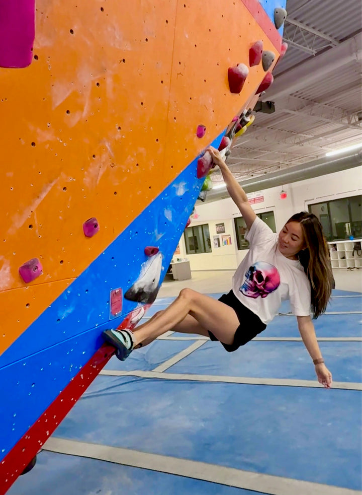 Model climbing indoor rock wall and wearing Skull Style Cropped Tee – White Short Sleeve Crop Top with Skull Design