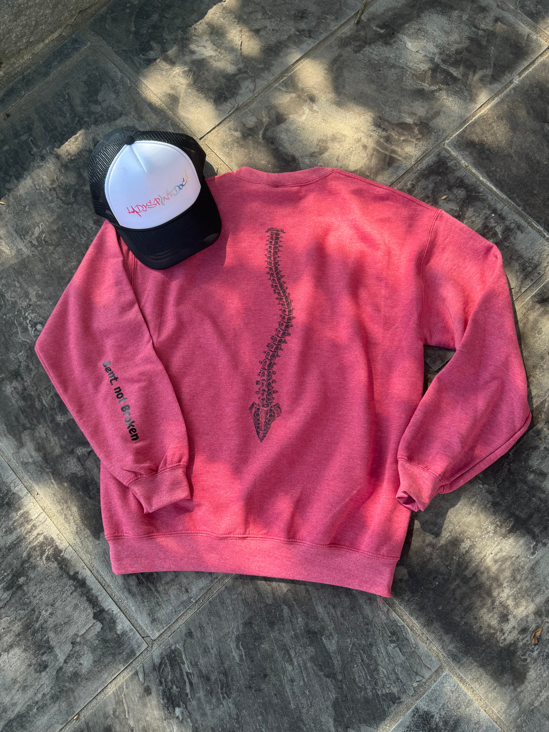 Flat lay of the back of the Bent Not Broken Scoliosis Crewneck Sweatshirt – Heather Red showing the spine design. The sleeve is flipped back to show off the Bent, not Broken motto.