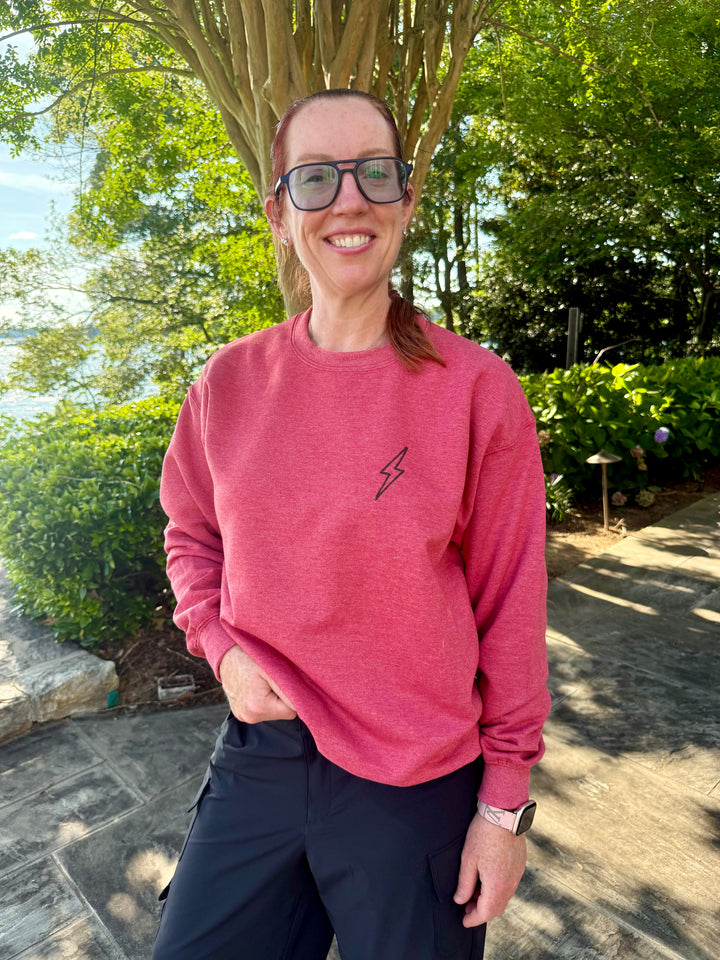 Ladyspinedoc modeling her Bent Not Broken Scoliosis Crewneck Sweatshirt – Heather Red, showing the front lightning bolt detail on upper left chest.