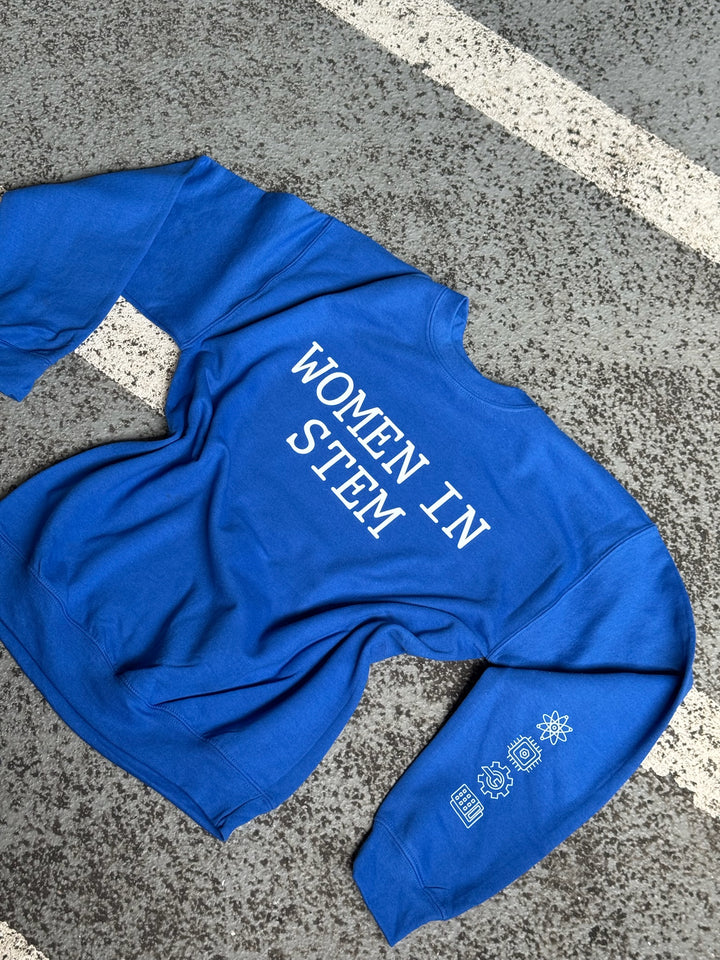 “Women in STEM” Sweatshirt laid flat on pavement and showing the STEM icons of Science, Technology, Engineering, and Mathematics on the left sleeve.