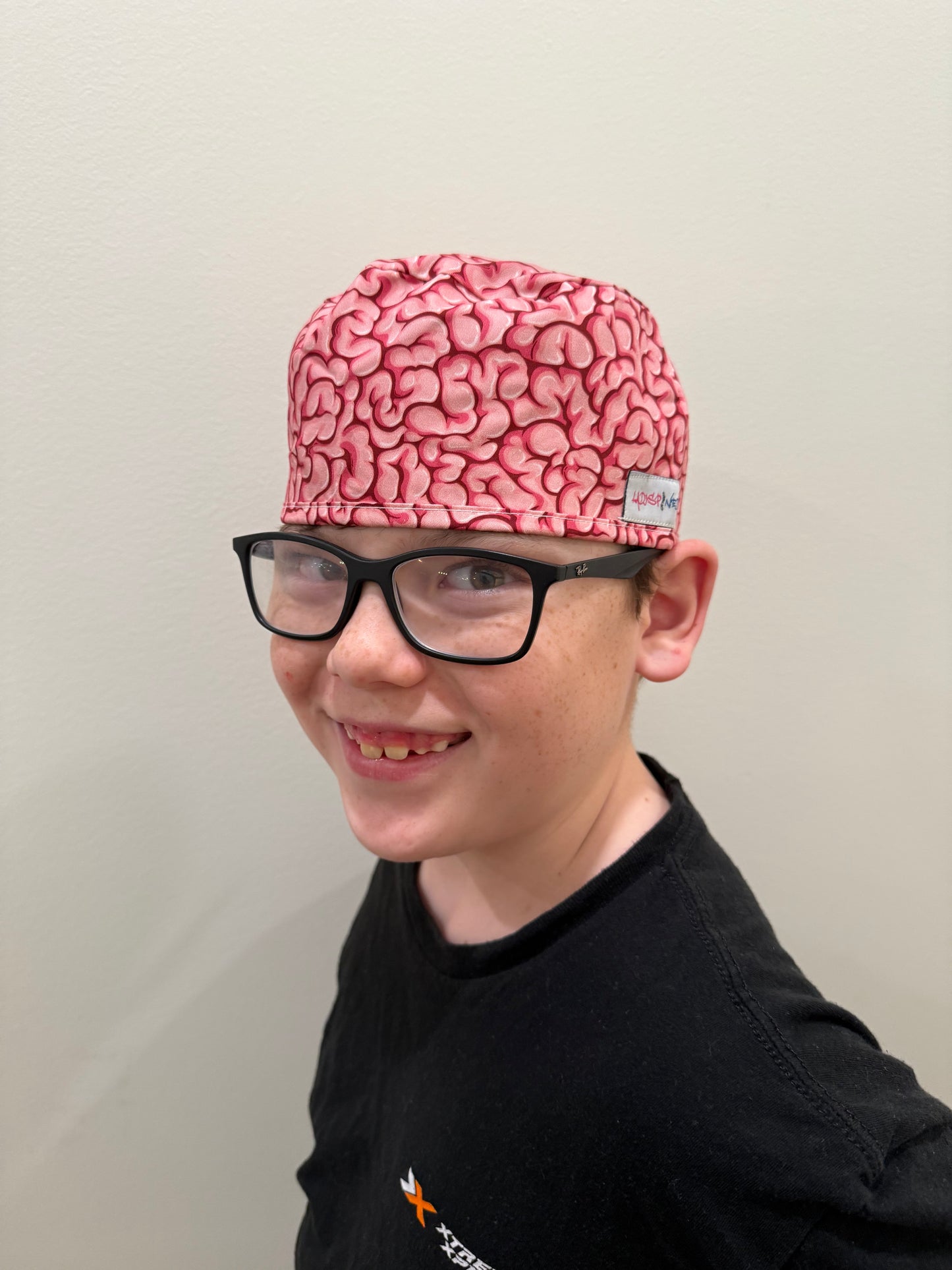 Front view of a youth wearing the tie-back (short hair) version of the Cortex Cap - Pink Scrub Hat with Brain Design