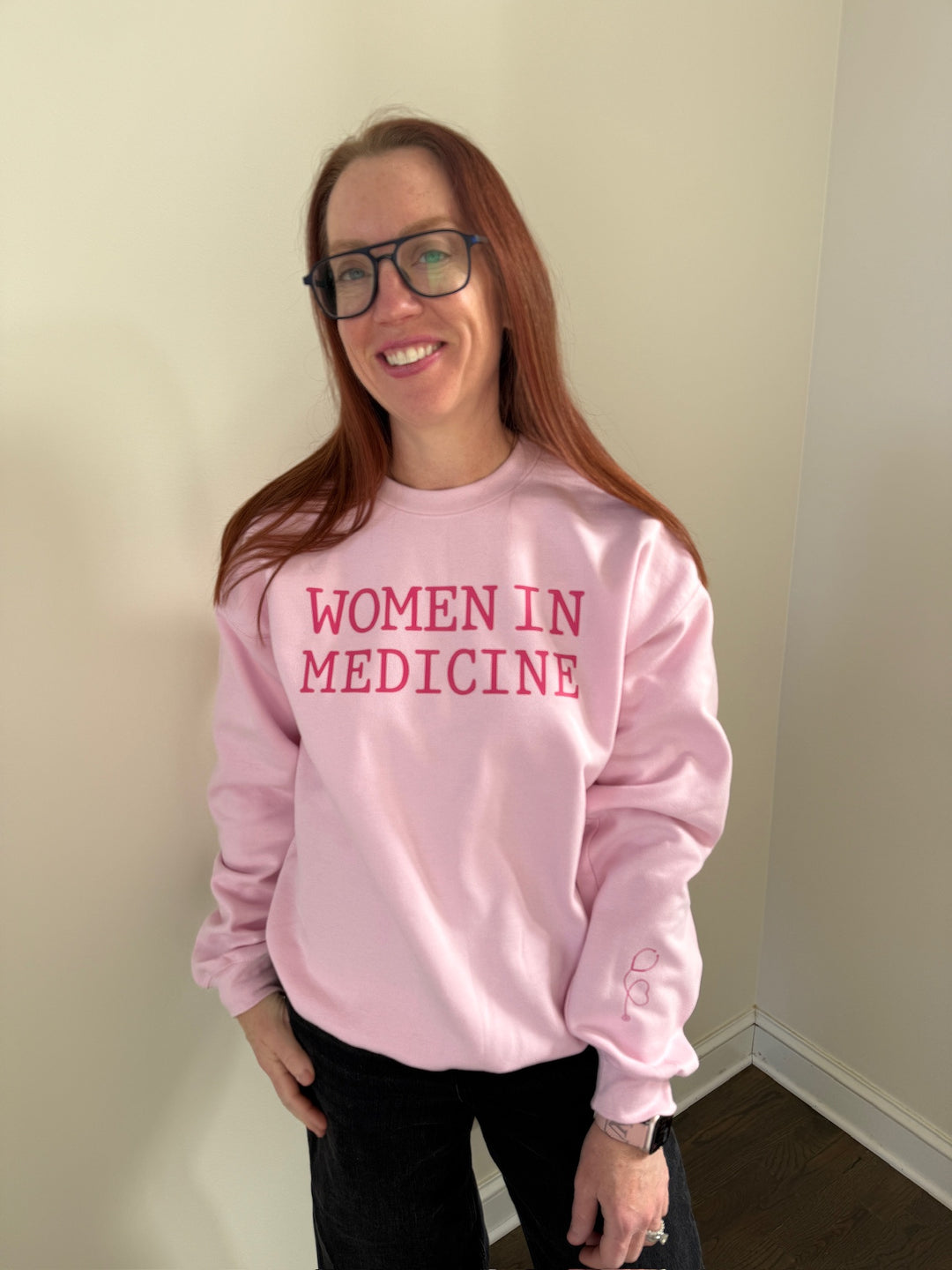 Dr. Betsy Grunch - Ladyspinedoc wearing light pink “WOMEN IN MEDICINE” sweatshirt, showcasing the left sleeve with heart-shaped stethoscope design.