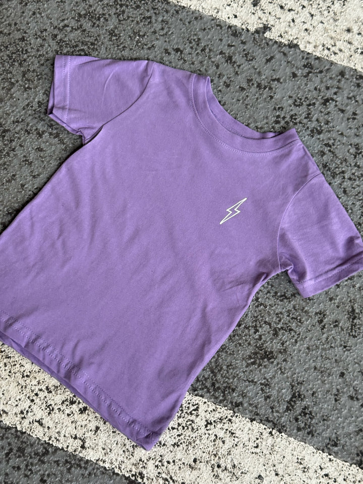 Flat lay of purple toddler tee with Ladyspinedoc lightning bolt on left chest on pavement.
