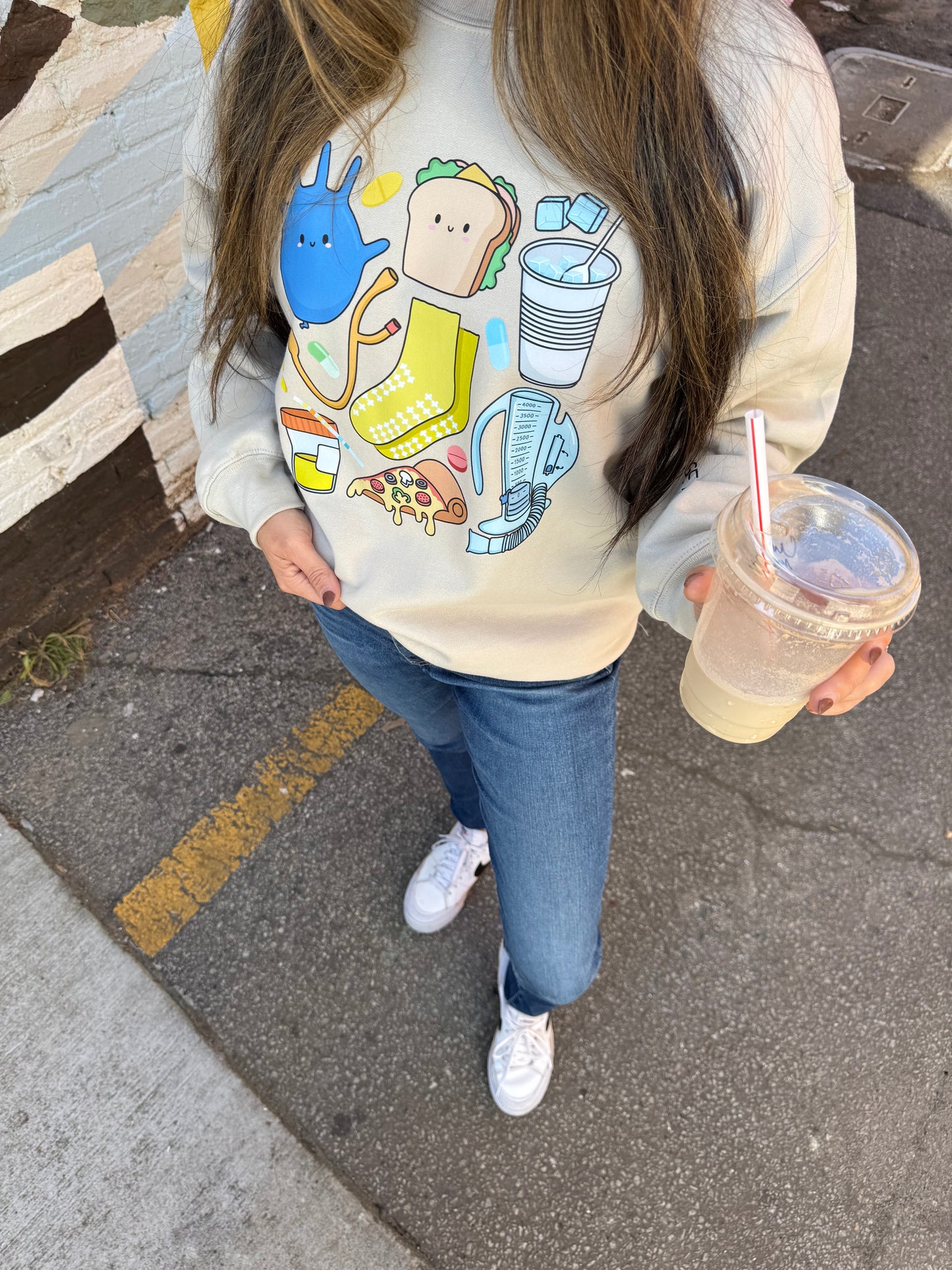 Close up of beige Nurse Sweatshirt with cartoon nurse memorabilia on the front.