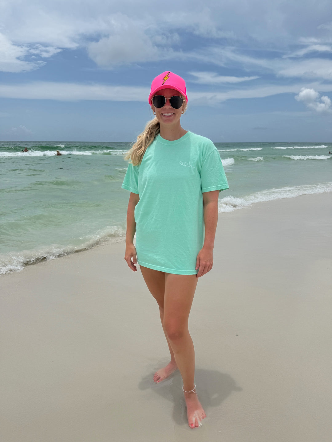 Woman at beach wearing the Island Reef light green Heart of Medicine t-shirt featuring Dr. Beachgem’s stethoscope and heart waveform logo on the upper left chest.