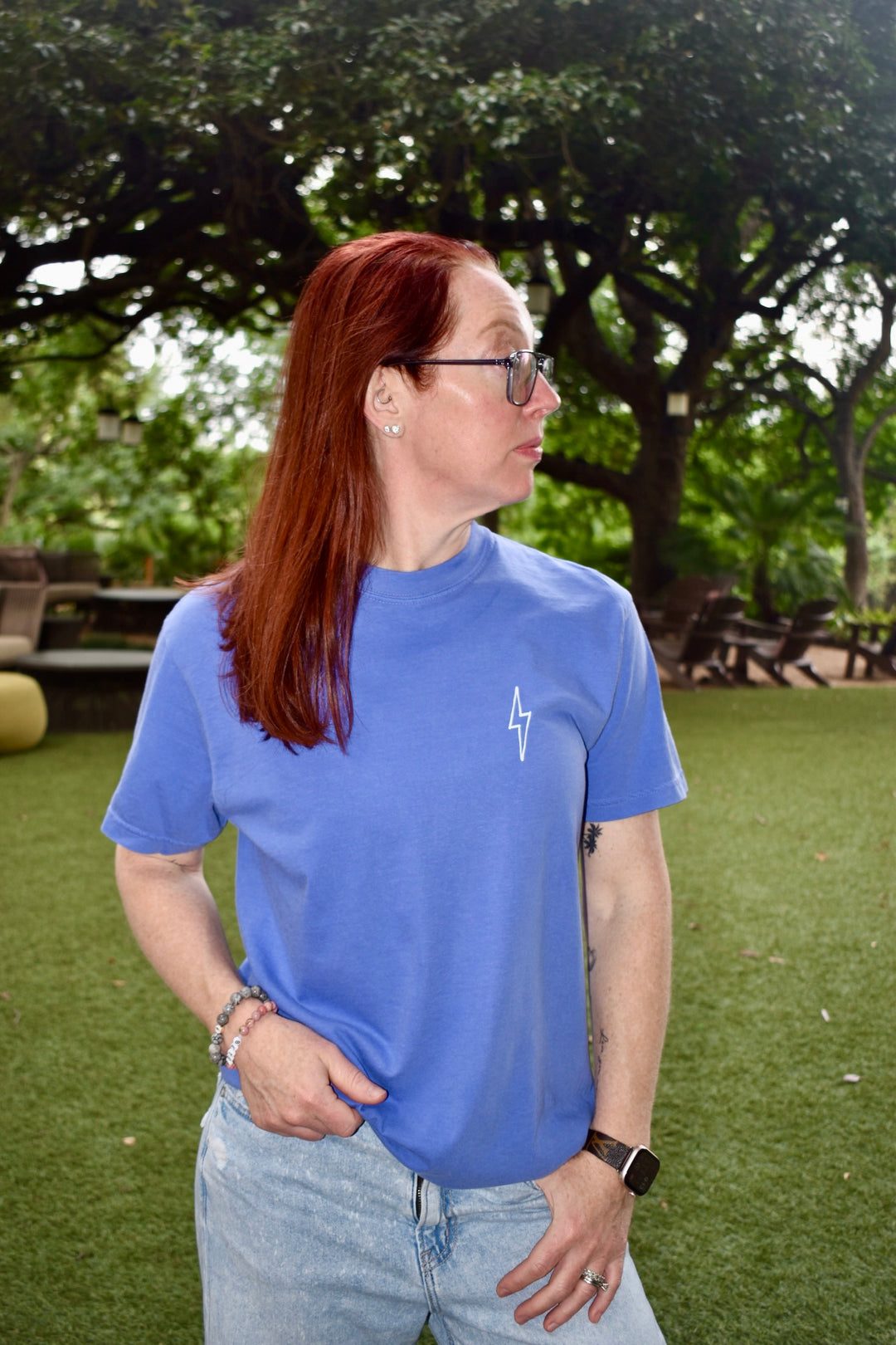 Ladyspinedoc wearing The Incredible Tee in purple, standing confidently outdoors in wooded setting.