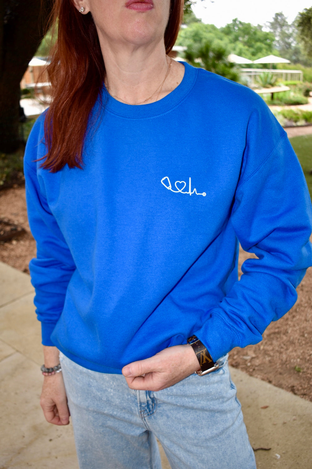 Front view of Dr. Betsy Grunch (Ladyspinedoc) wearing the Heart of Medicine sweatshirt in royal blue with her holding the bottom hem.