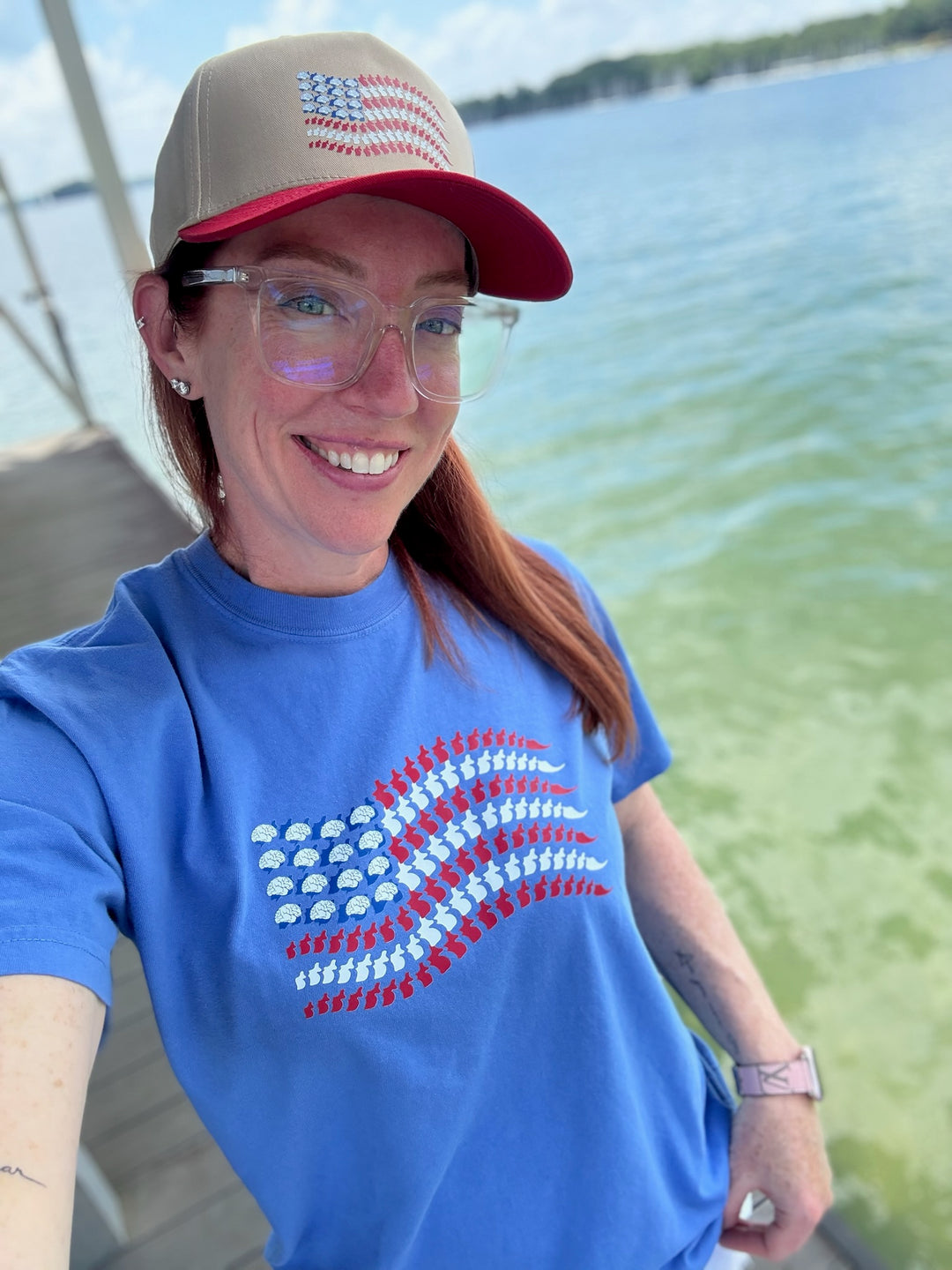 Ladyspinedoc smiling in a blue Stars, Stripes & Synapses tee featuring brains and spines as a patriotic flag, by the lake.