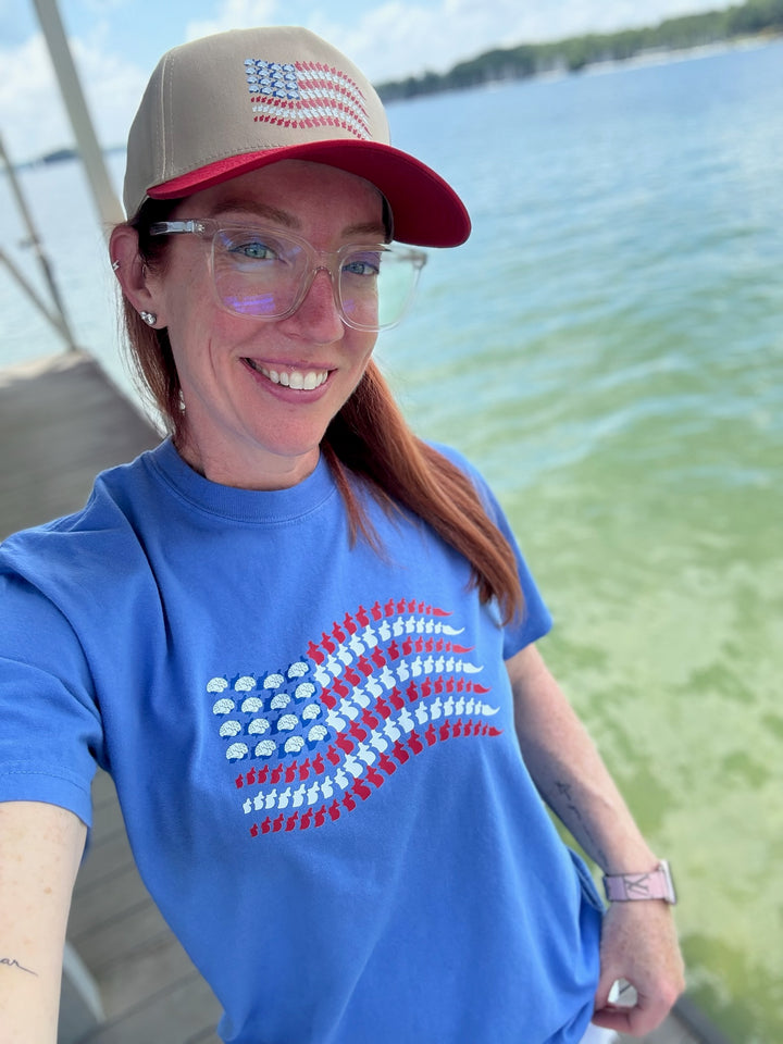Ladyspinedoc smiling in a blue Stars, Stripes & Synapses tee featuring brains and spines as a patriotic flag, by the lake.