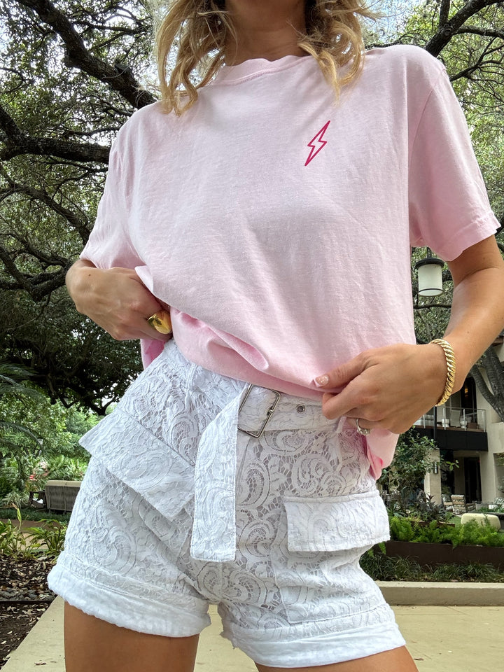 Woman wearing a light pink t-shirt with a small hot pink lightning bolt on the chest and lace shorts.