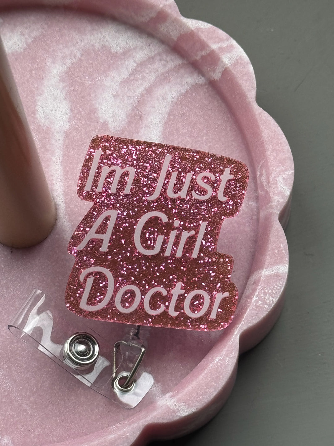 Retractable glitter pink badge reel that says “I'm Just A Girl Doctor.” in a pink tray.