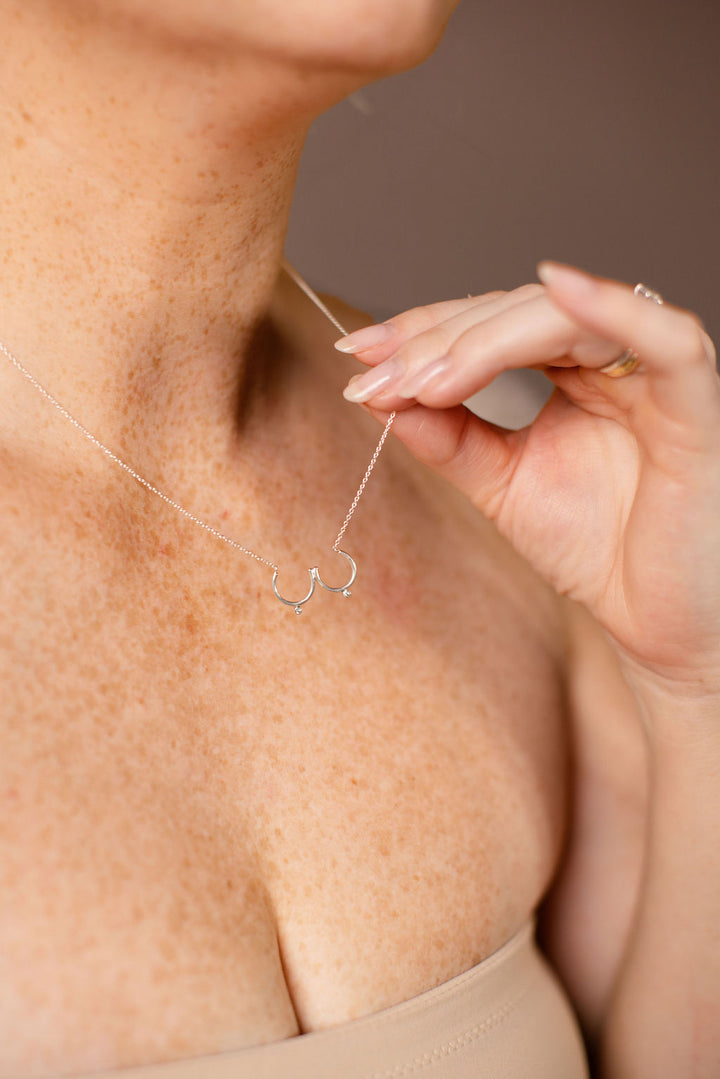 Model holding up silver Bust Necklace with Diamond Nipples from her neck