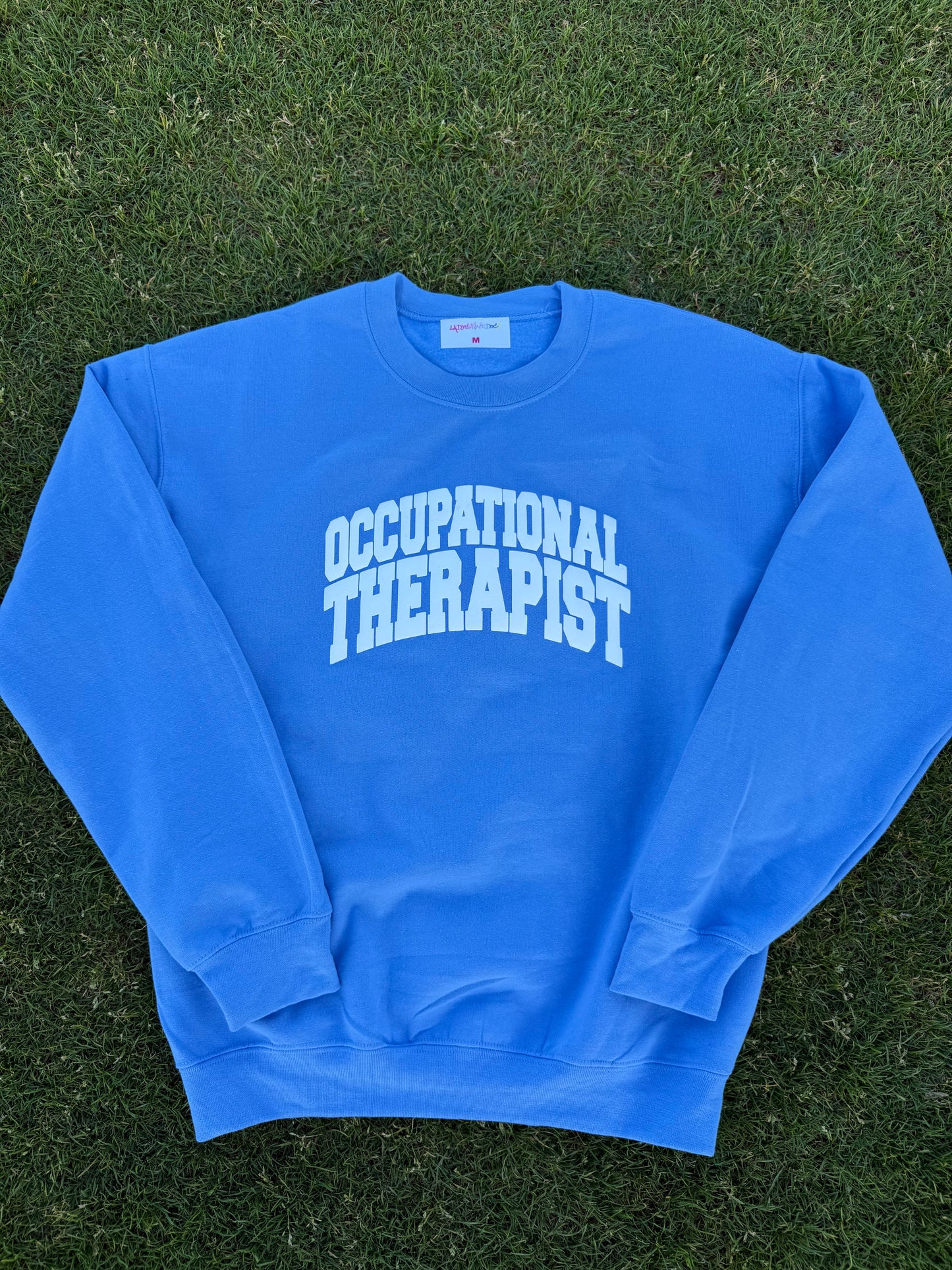 Flat lay of the blue Occupational Therapist crewneck sweatshirt designed by Ladyspinedoc (Dr. Betsy Grunch)