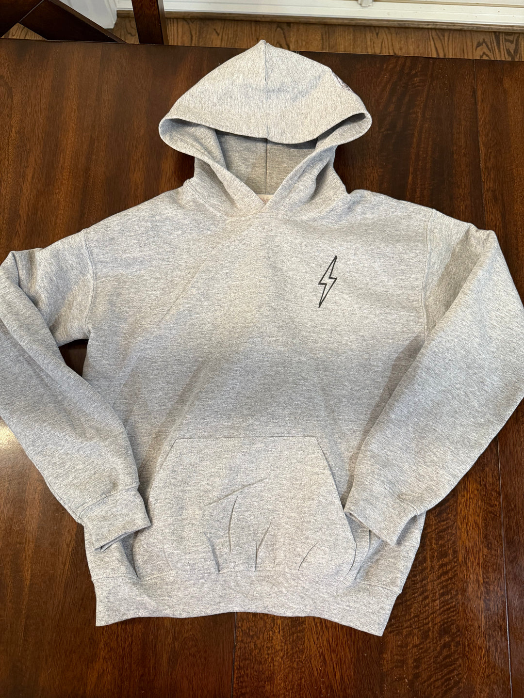 Light gray hoodie with a black lightning bolt on the upper left chest and kangaroo pocket.