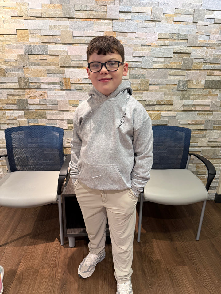 Child model wearing light gray hoodie with a black lightning bolt on the upper left chest and kangaroo pocket.