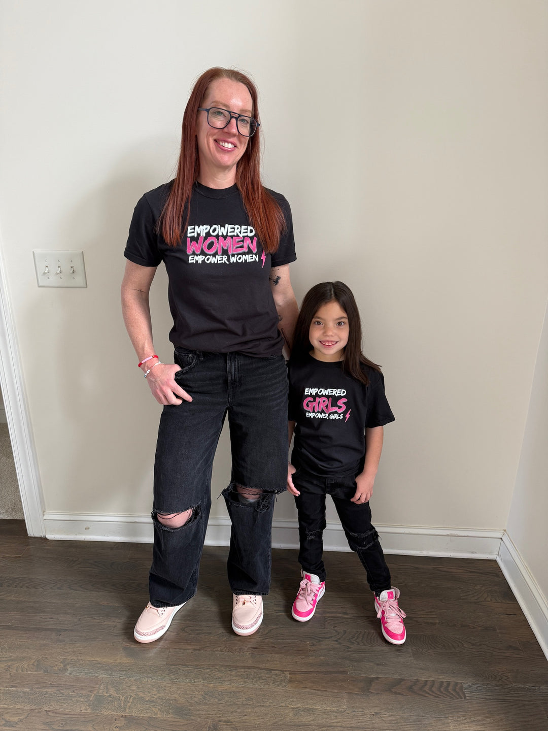 Dr Betsy Grunch (Ladyspinedoc) and her daughter wearing matching black tee shirts. Betsy's shirt says, "Empowered women empower women." Her daughter's shirt says, "Empowered girls empower girls."