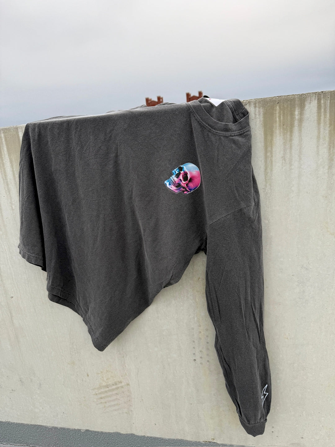 Skull Powers Long Sleeve Tee Shirt - Dark Gray with Skull and Lightning Bolt Design laying on a concrete wall