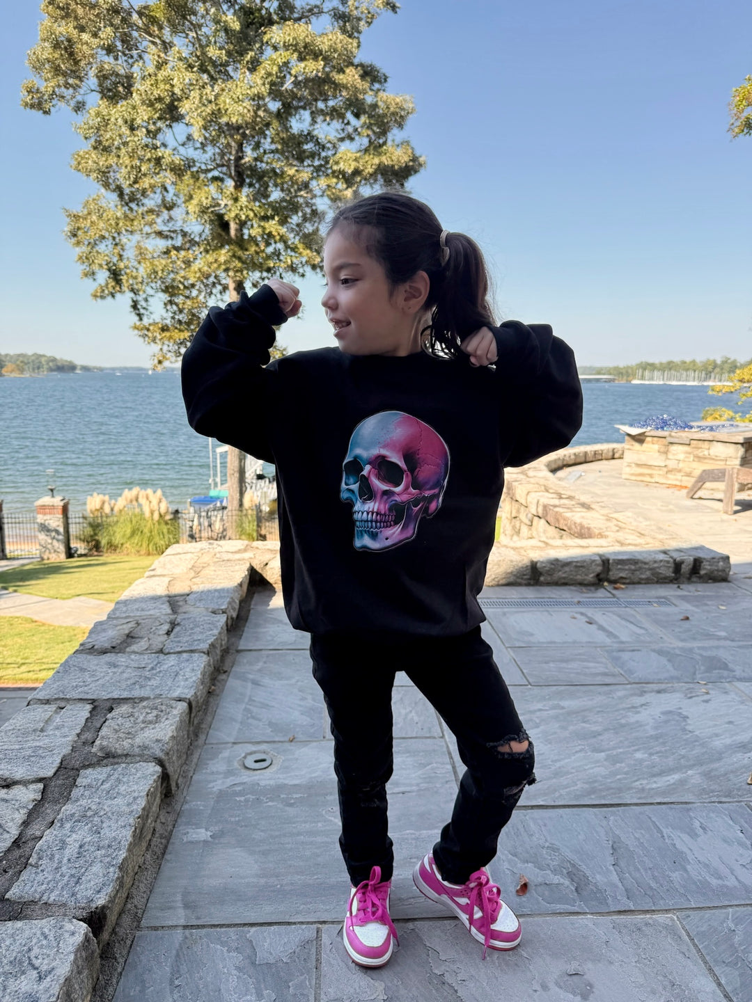 Young girl with arms up wearing the Super Skull Youth Crewneck Sweatshirt – Kids Black Pullover with Skull Graphic
