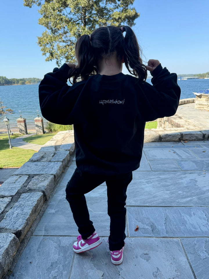 Girl showing off the back of the Super Skull Youth Crewneck Sweatshirt with lake in background