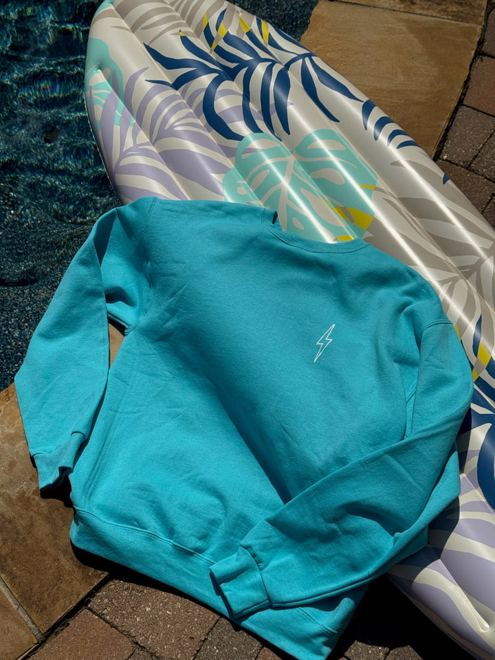 Teal sweatshirt on a tiled floor with a pool and inflatable raft in the background