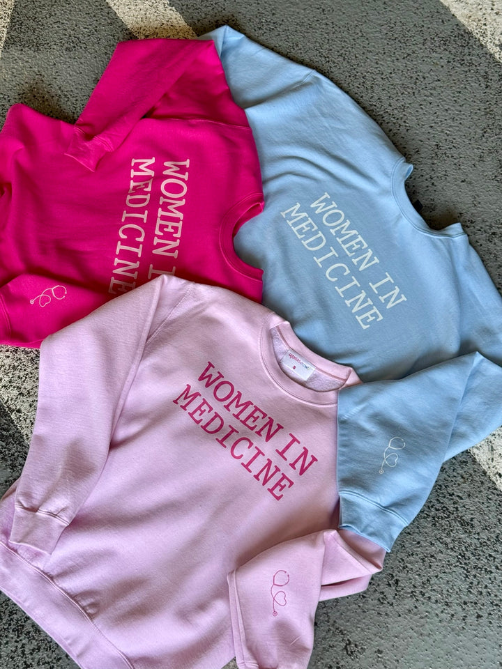 Three sweatshirts in hot pink, light blue, and light pink with 'Women in Medicine' on the front.