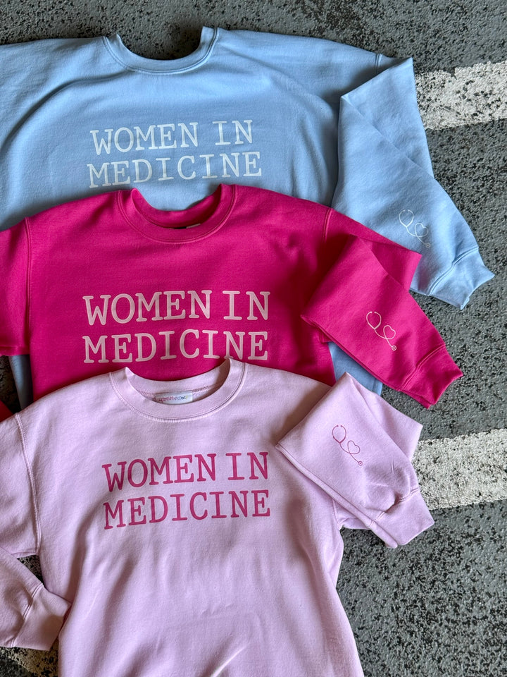 Light Pink, Light Blue, and Hot Pink Women in Medicine Crewneck Sweatshirts showing the Stethoscope Design on left sleeve.