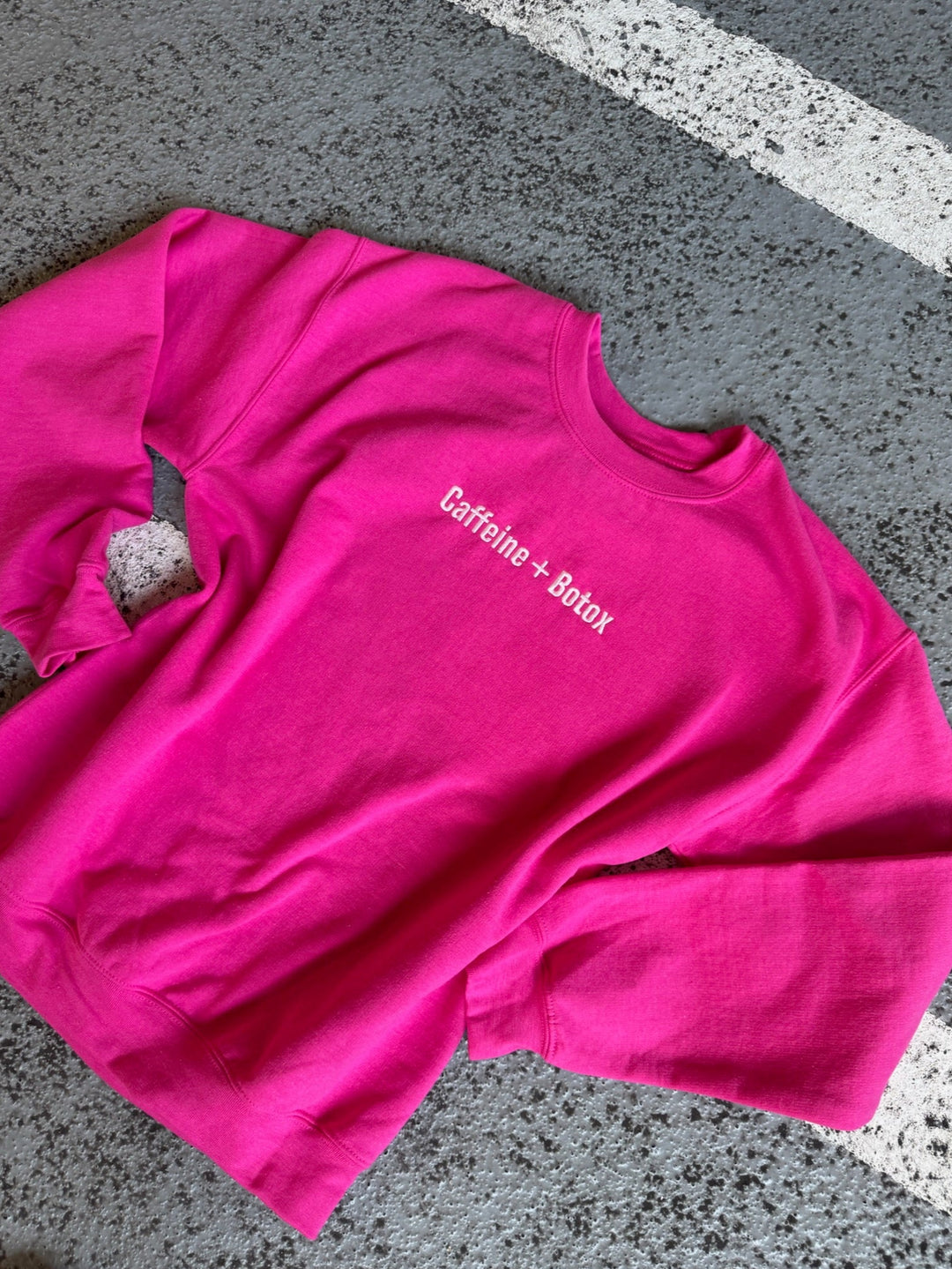 Pink sweatshirt with 'Caffeine + Botox' text on a gray pavement background