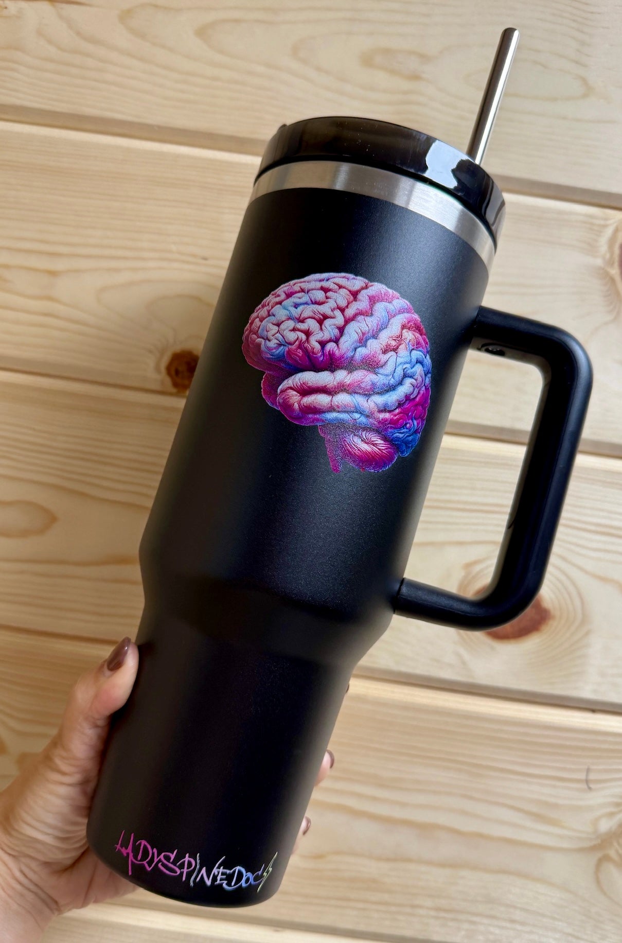 Hand holding the Big Brain Energy Cup to show the colorful brain design and the Ladyspinedoc logo at the base