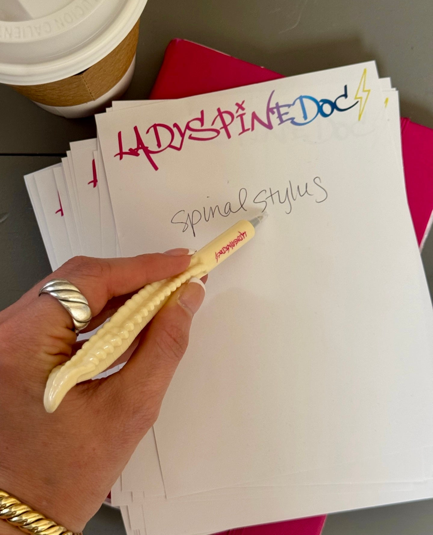 Woman's hand writing with a Spinal Stylus spine-shaped pen featuring vertebrae detail