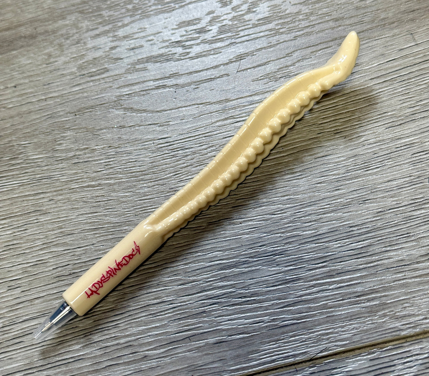 Close-up of the Spinal Stylus Pen resting on wood surface, showcasing spine design and hot pink logo.