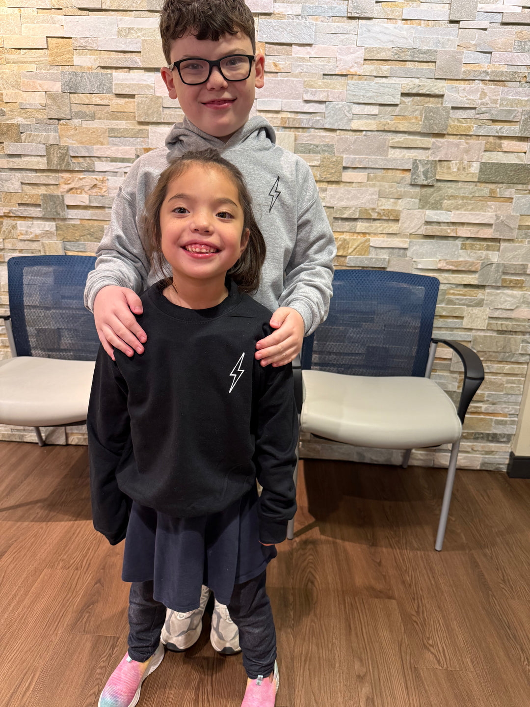 Girl youth model wearing the Incredible Youth Crewneck Sweatshirts, facing forward showing the lightning bolt on chest. Male youth model facing forward wearing the youth Big Brain Energy Sweatshirt showing the lighting bolt on chest.