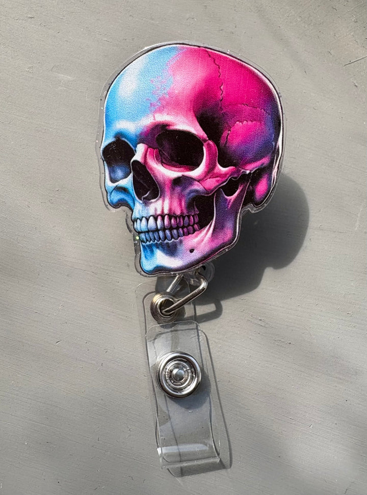 Retractable badge reel with colorful skull design in blue and pink colorful gradients with sparkles, attached to a clear plastic ID holder clip.