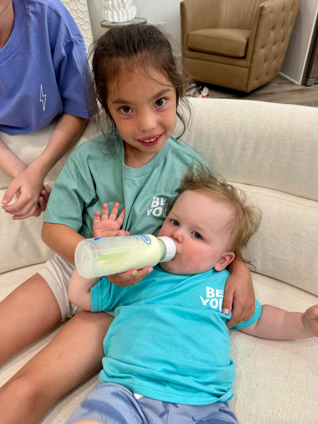 Toddler being bottle fed while wearing the Be You Toddler Tee - Kids Caribbean Blue T-Shirt with Motivational “BE STRONG. BE KIND. BE YOU.” Motto