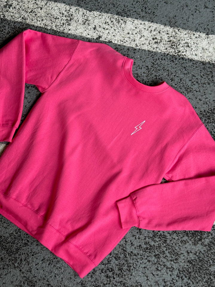 Flat lay of Ladyspinedoc pink crewneck sweatshirt on asphalt, showcasing subtle white lightning bolt logo on chest.