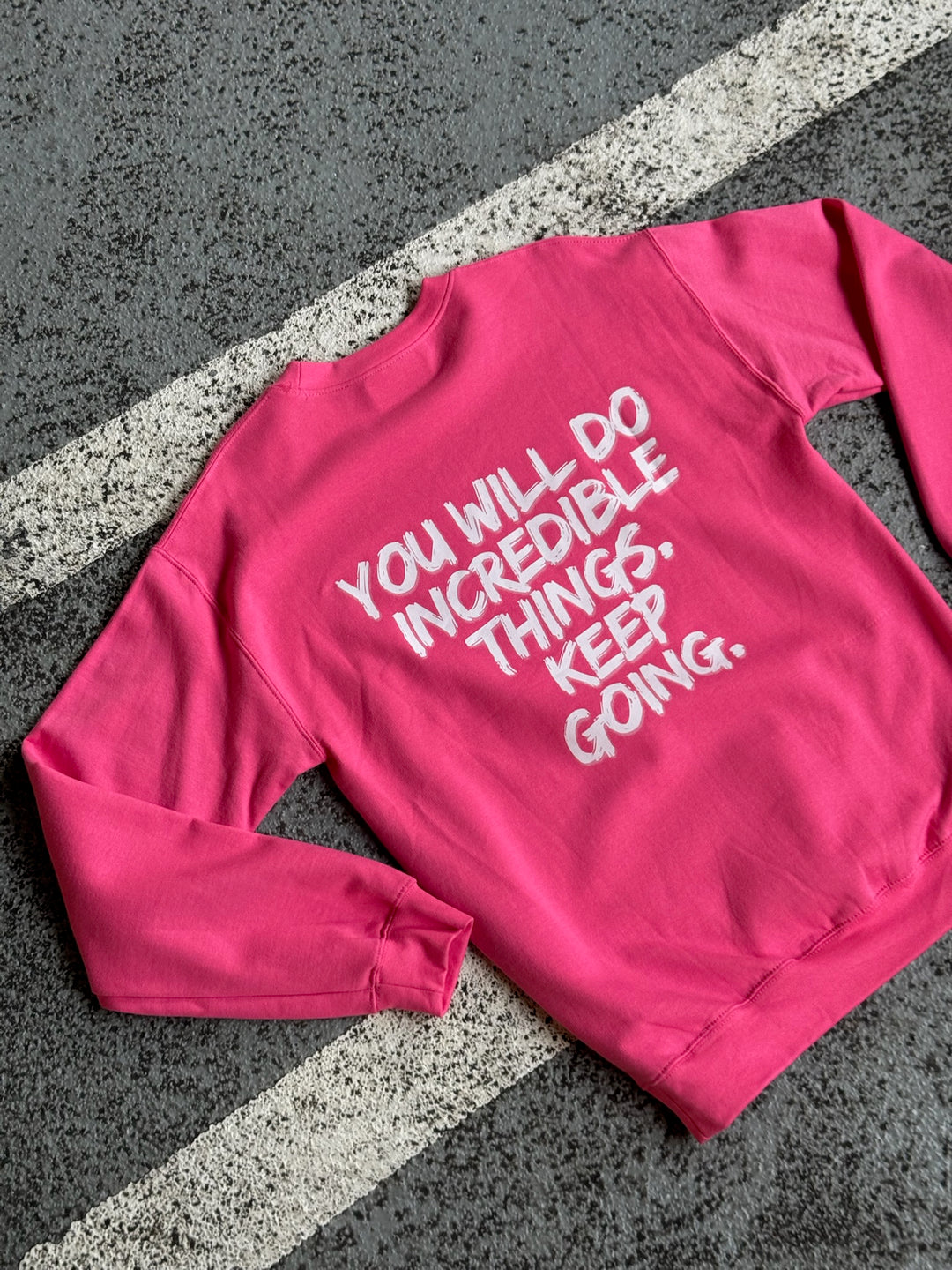 Back of Ladyspinedoc “Incredible” sweatshirt displayed on asphalt, with bold motivational message printed in white: “YOU WILL DO INCREDIBLE THINGS. KEEP GOING.”